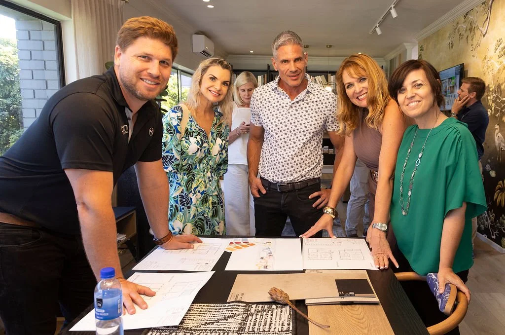 Group of six people smiling and gathered around a table with papers and design samples in a well-lit room. Erica from Birdsye Digital. Marco and Gary from Como Flooring and Kim Williams from KWD