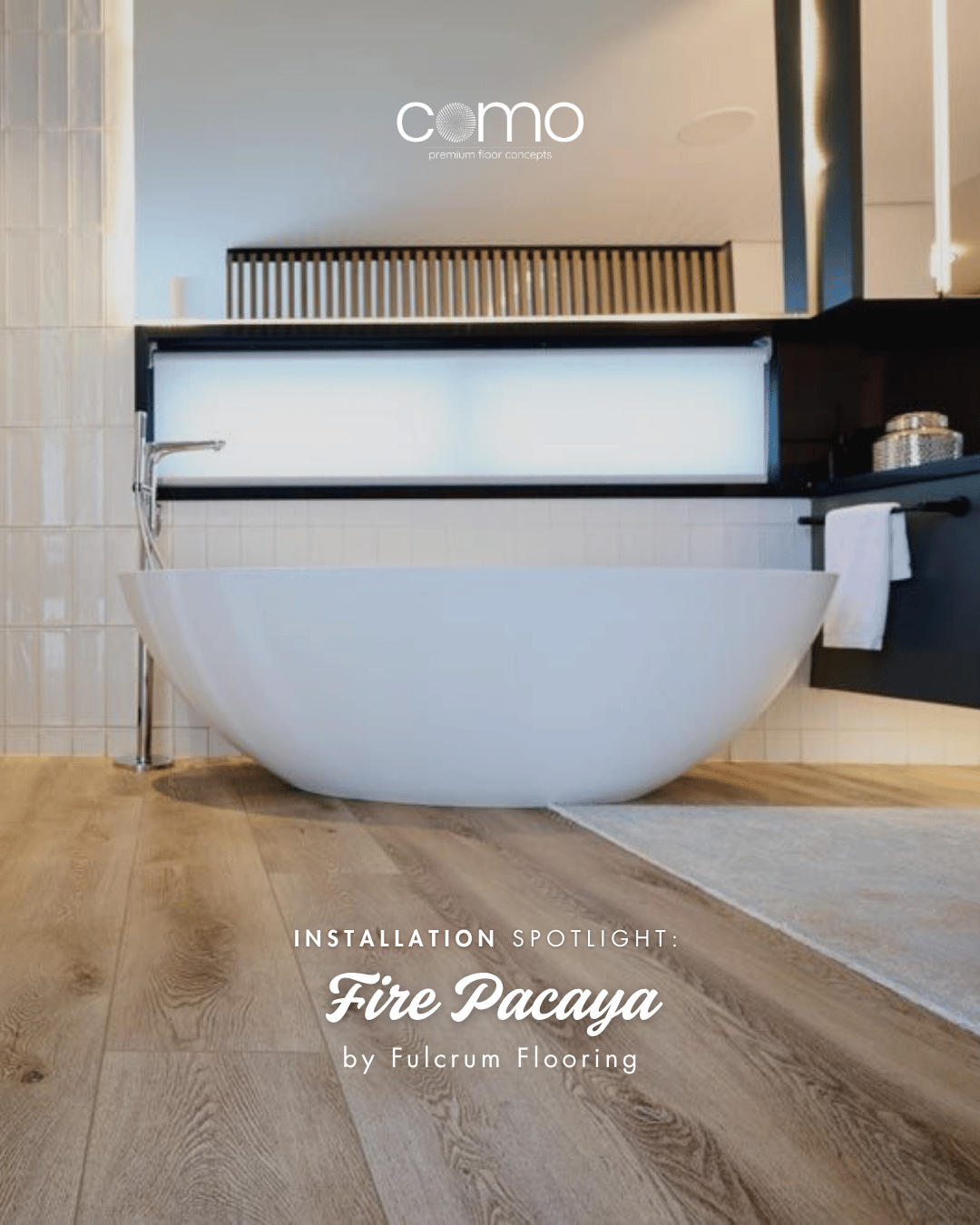 Modern bathroom with a white freestanding bathtub, wooden flooring, and black accents. There is a towel hanging on a black towel bar, and shelves with decorative items in the background. Featuring Como Flooring Fire Pacaya Vinyl Flooring