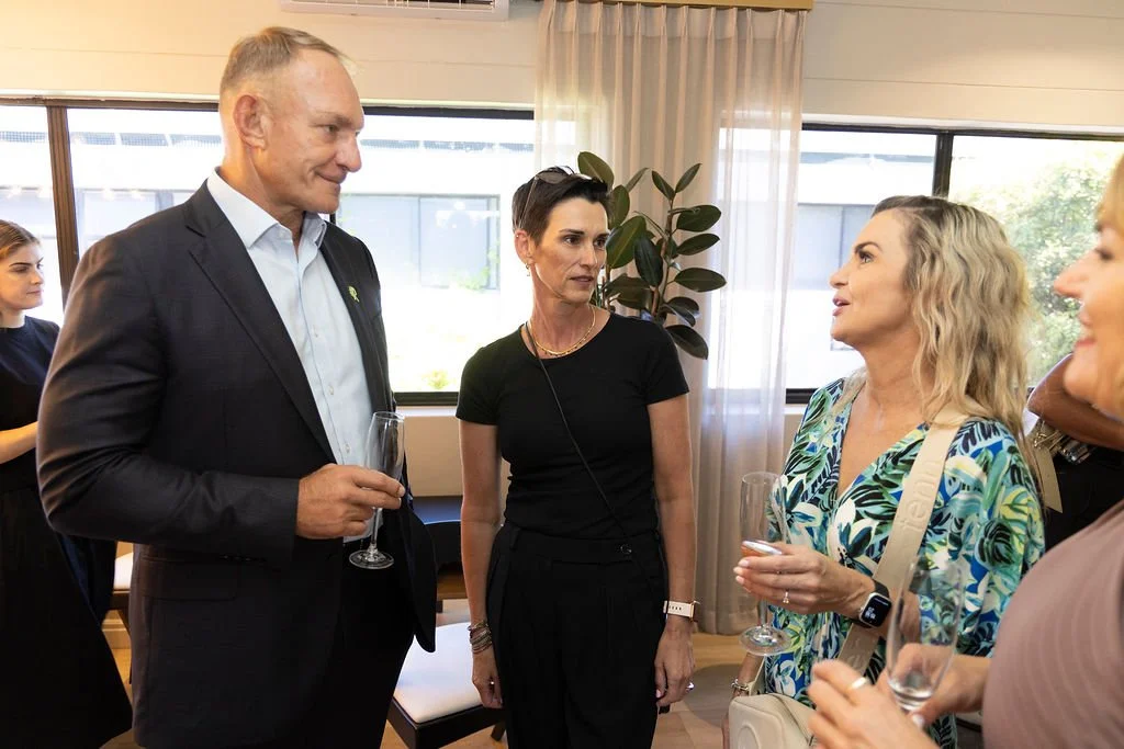 Group of people conversing at a social gathering, holding glasses of champagne, with a background of large windows. With Annemarie from Hertex, Erica from Birdseye Digital and Francois Pienaar the ex rugby player and his The MAD Foundation