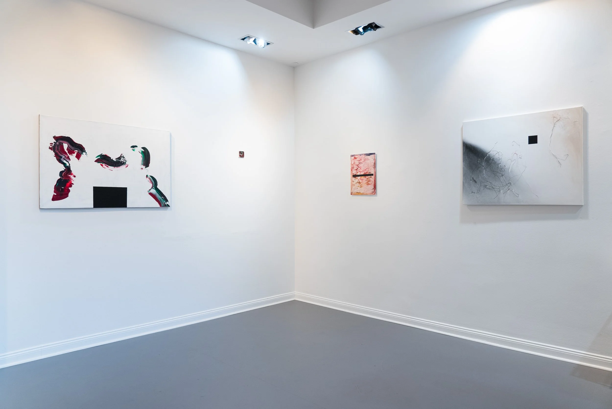Art gallery with three abstract paintings on white walls, featuring bold colors and swirling designs, with ceiling lights illuminating the artwork.