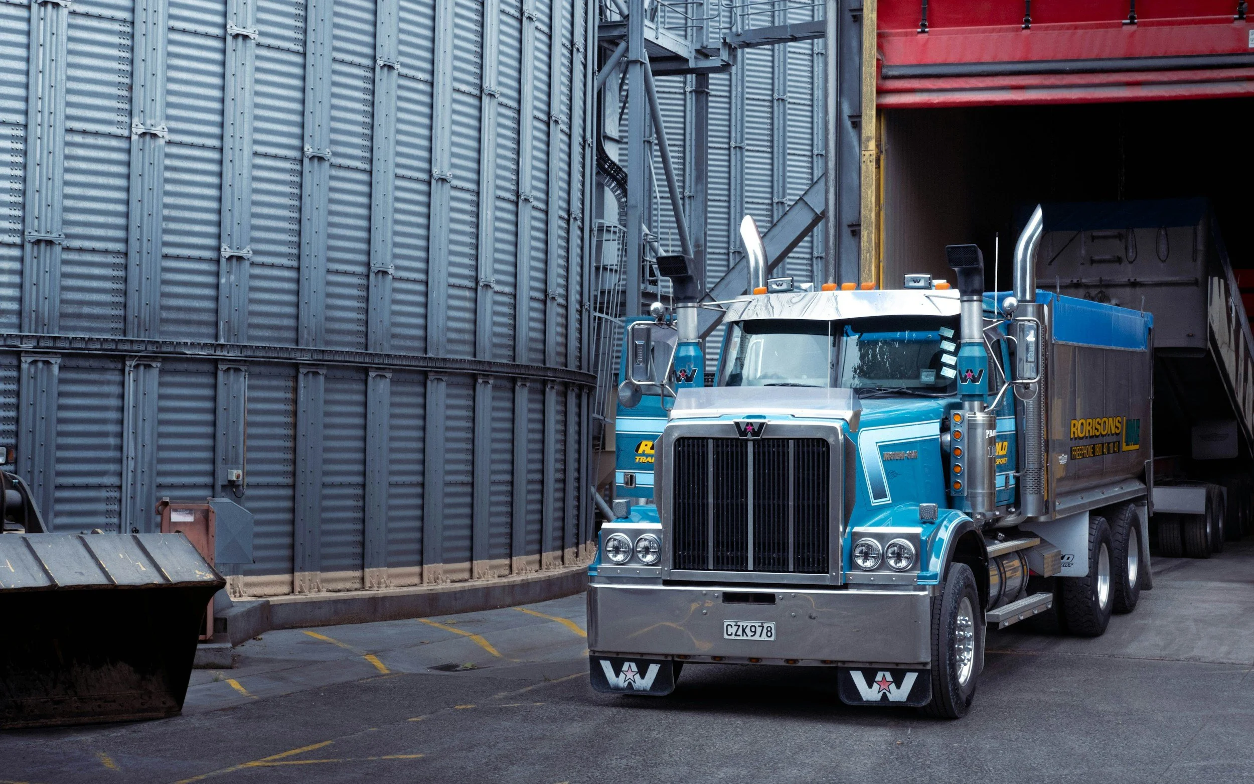 Un camion bleu dans un depot de fret avec des murs en métal, prêt à charger ou décharger des marchandises.