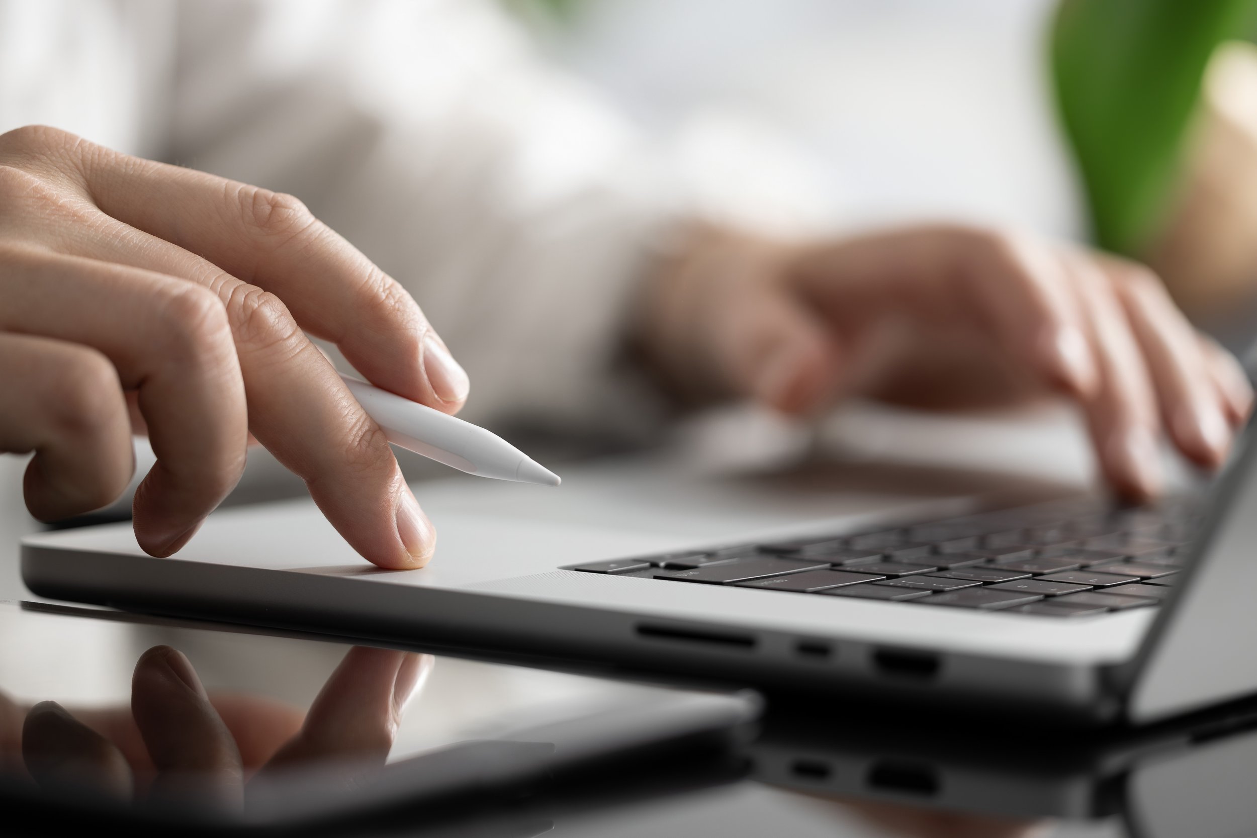Close-up of a person using a white stylus to operate a laptop keyboard, with a blurred background.