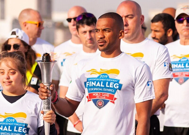 Man holding a torch at a relay event with multiple participants wearing white shirts with a 'Final Leg' logo for special Olympics in Abu Dhabi, 2019.