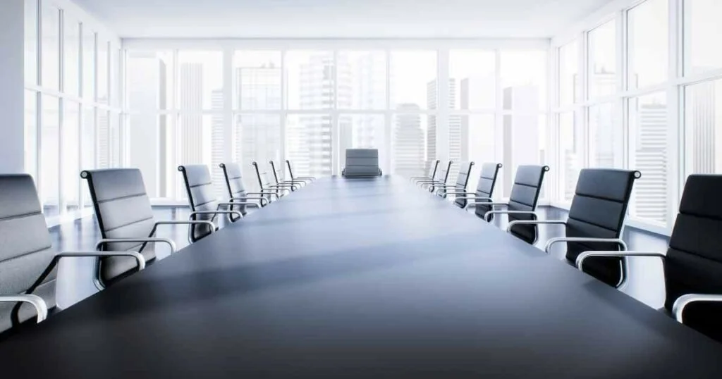 A modern, empty conference room with a long black table, black chairs, and large windows showing a city skyline.