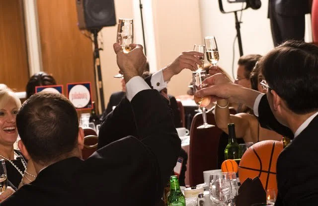 People in formal attire raising champagne glasses in a toast at a celebration event.