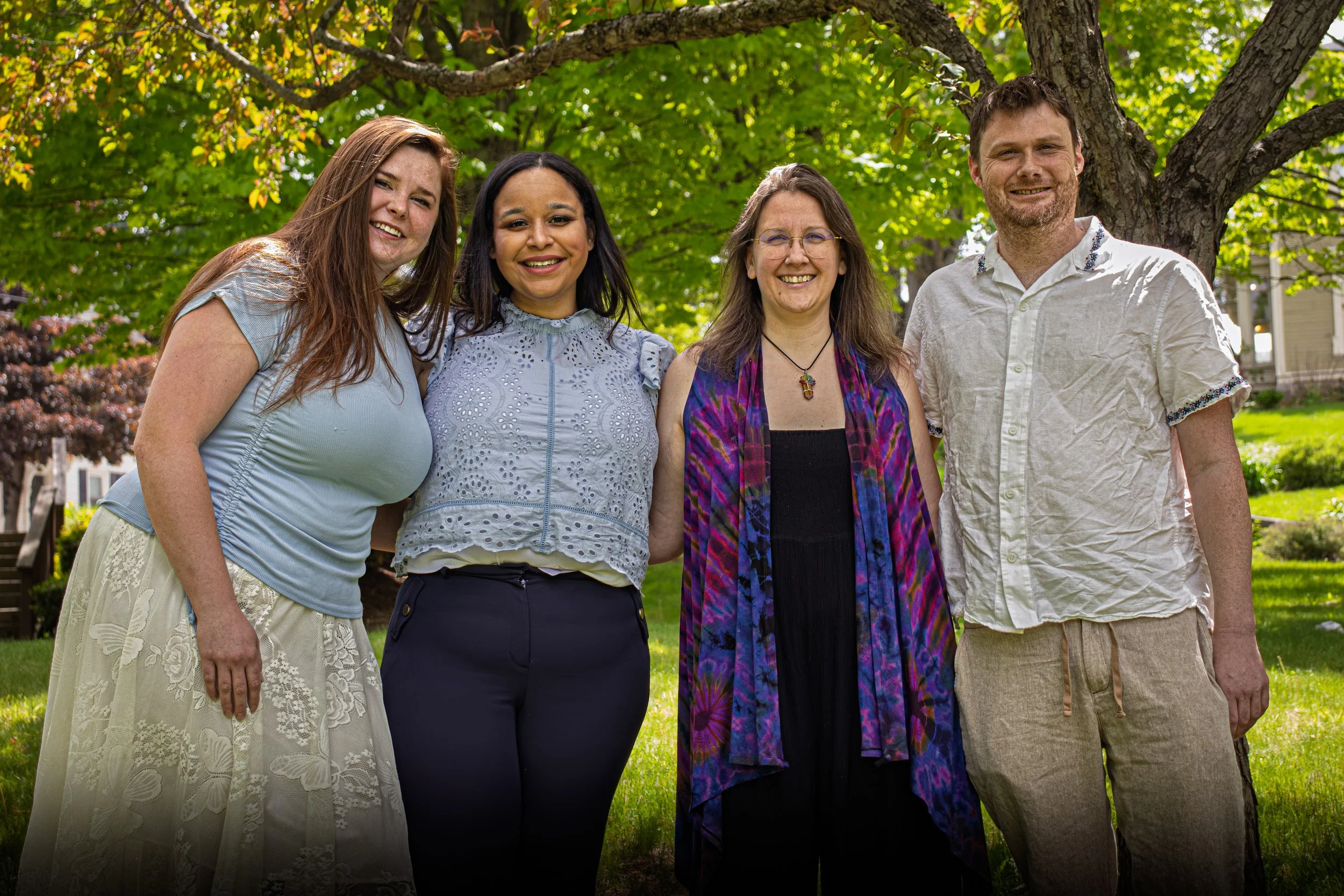 Group of four people outdoors standing under a large tree, smiling.
