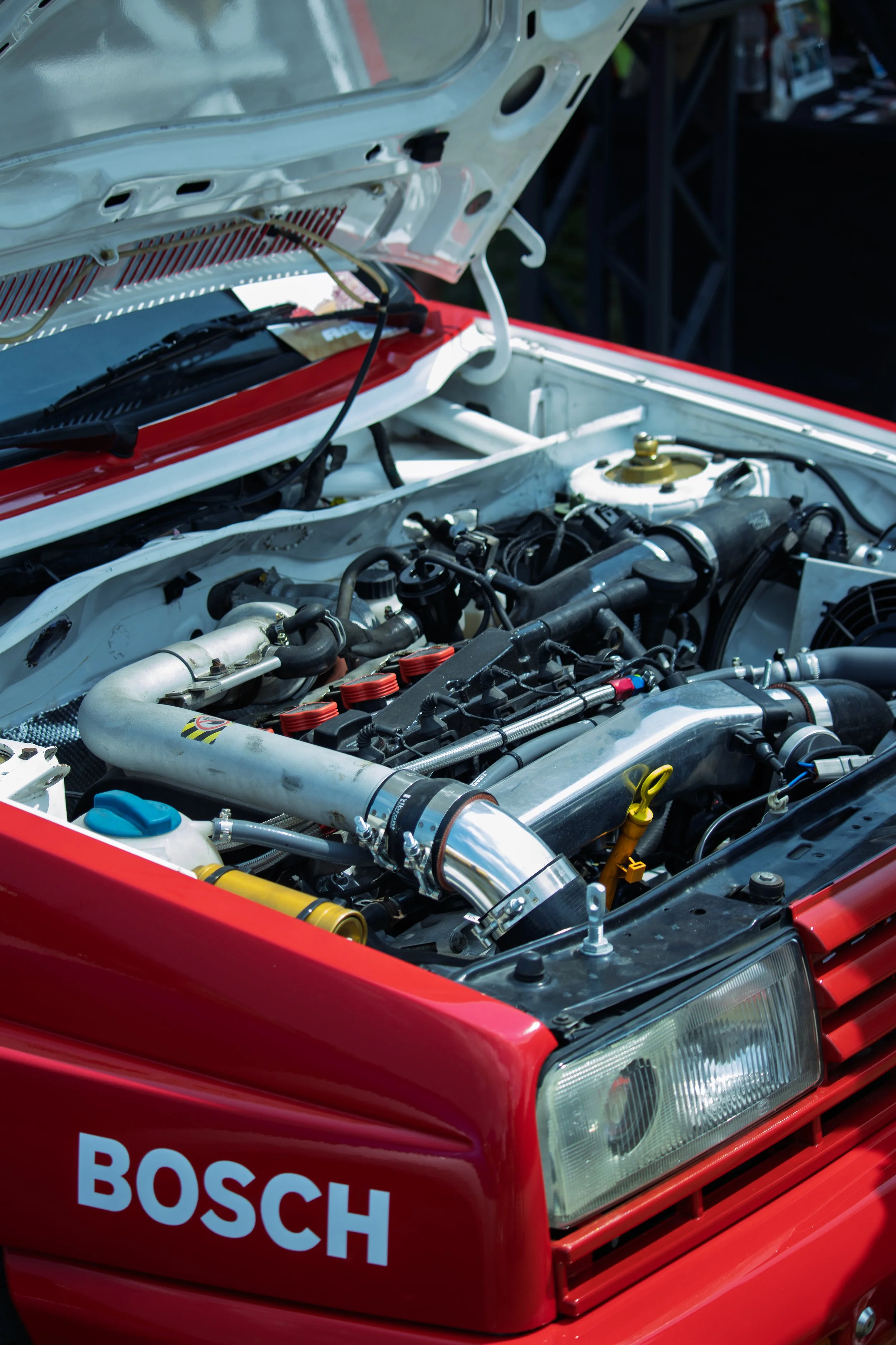 A red car with its hood open, revealing the engine and various mechanical components.