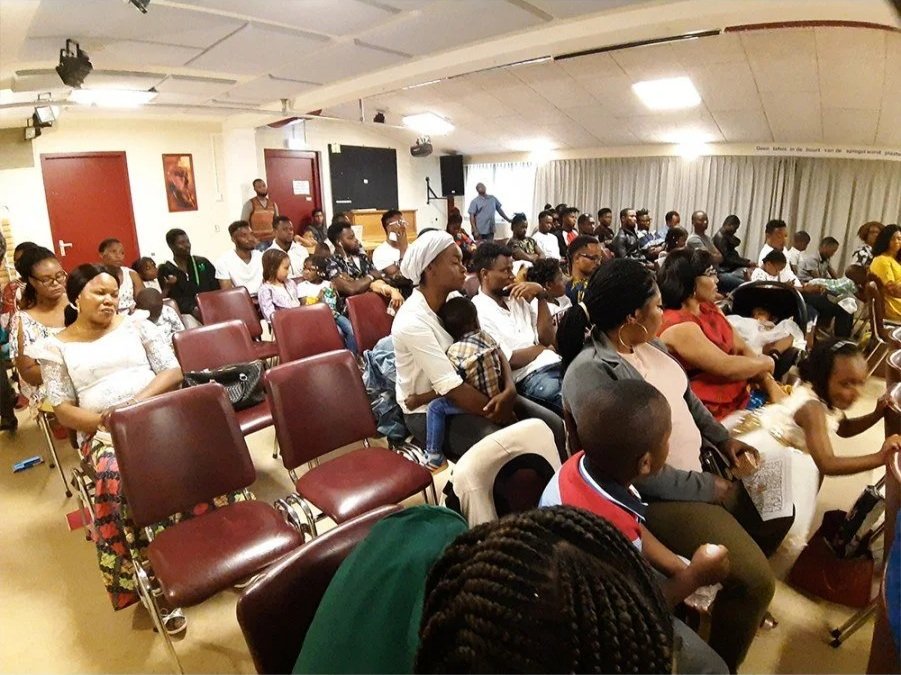 Group of people sitting in chairs inside a room, attending an event or presentation.