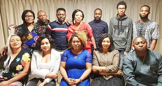 Group of people posing together in a room with curtains in the background.