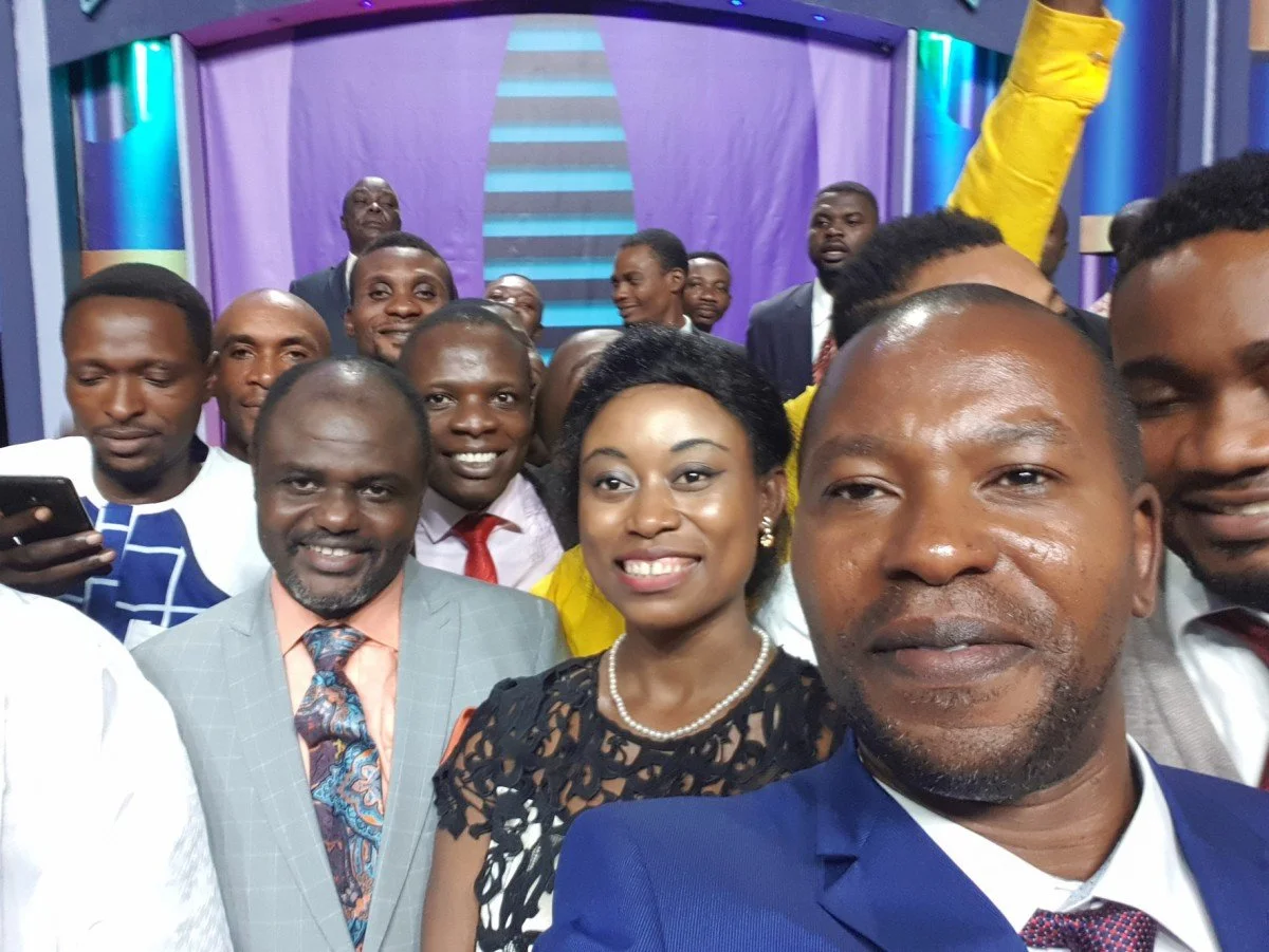 Group of well-dressed people taking a selfie on a colorful stage.