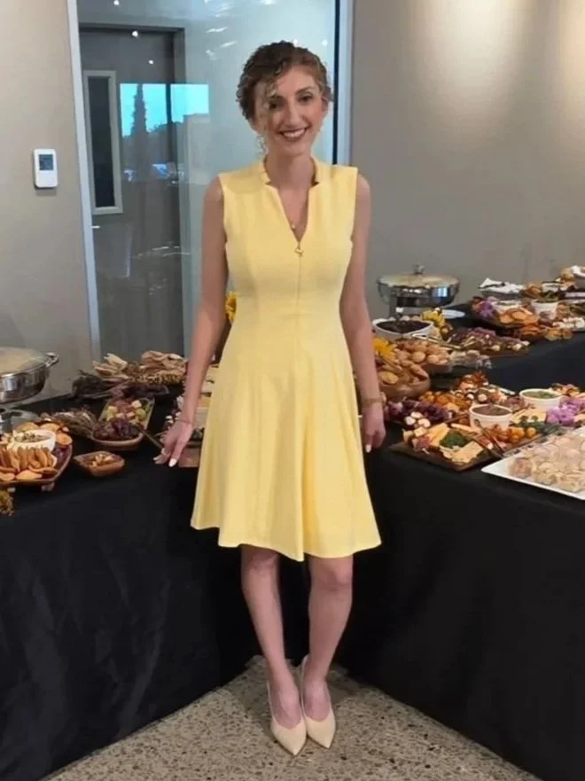 A woman in a yellow dress standing in front of a table with various food items at a buffet.