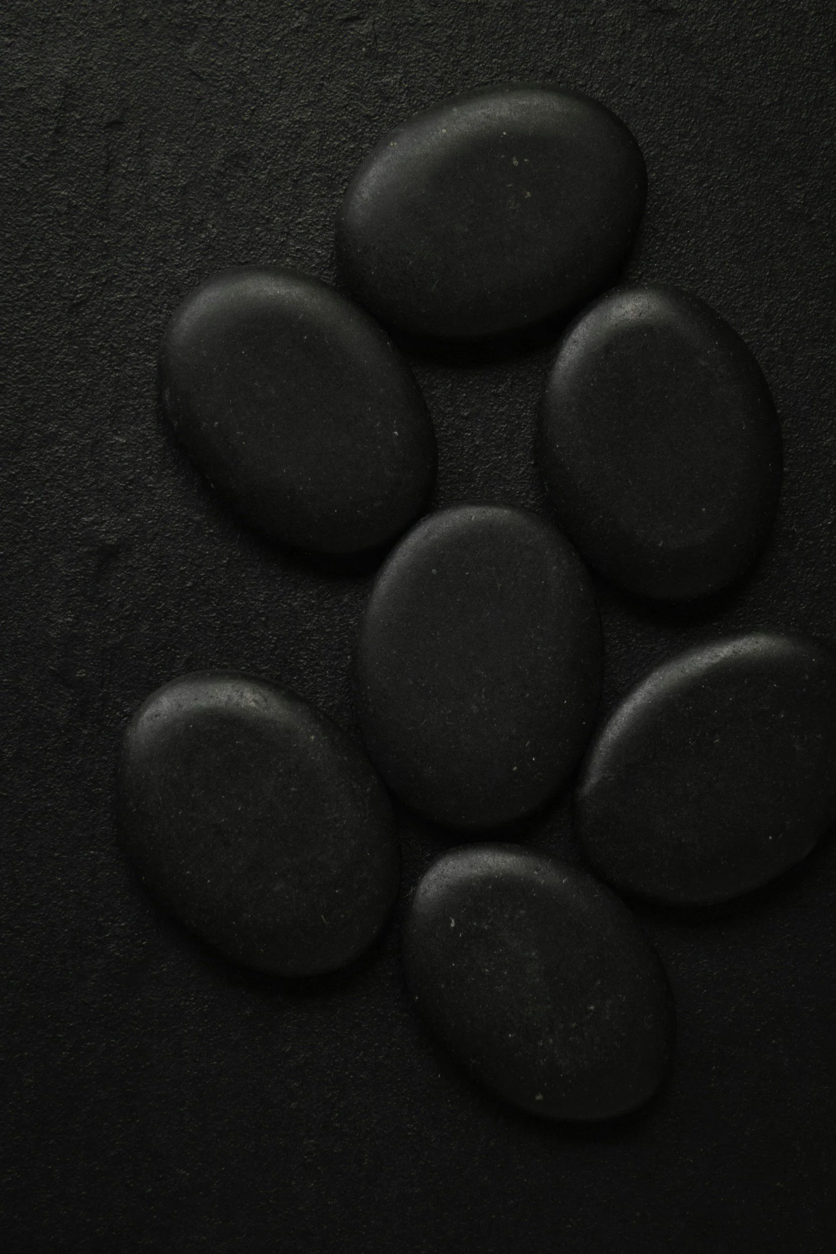Close-up of several black massage stones placed on a textured black surface.