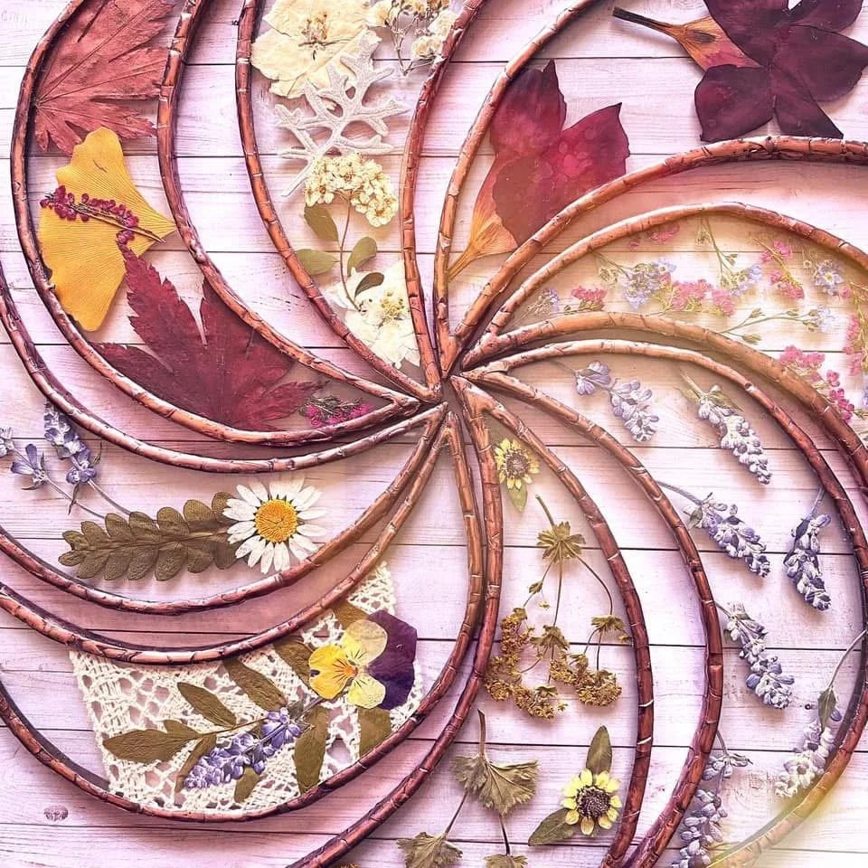Multiple heart-shaped wooden frames filled with pressed and dried flowers, arranged on a pink wooden surface.