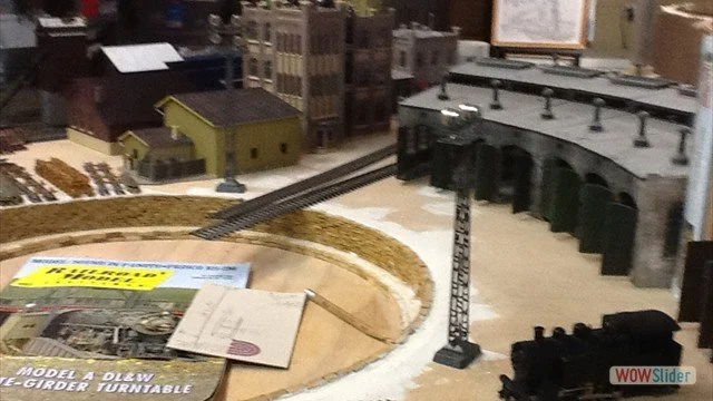 Model train set on a miniature landscape with buildings and tracks.