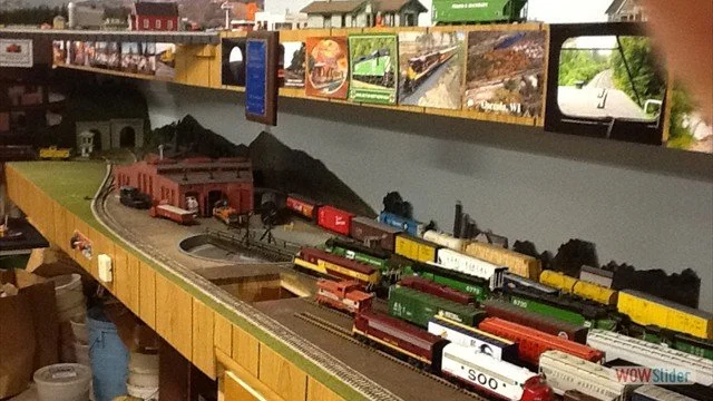 Model train set on a train layout with multiple connected train cars and a miniature landscape, displayed in an indoor setting.