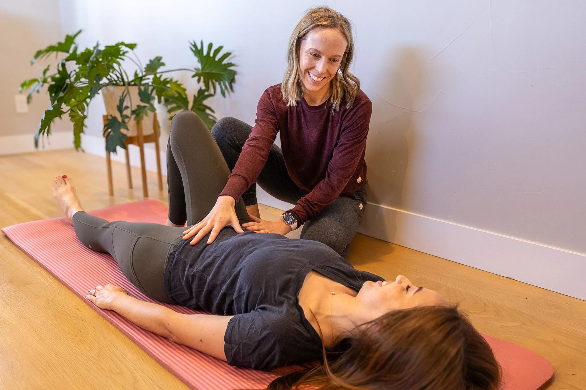 Dr. Emma Long is performing pelvic floor physical therapy, stretching, and relaxation exercises with a person lying on a yoga mat