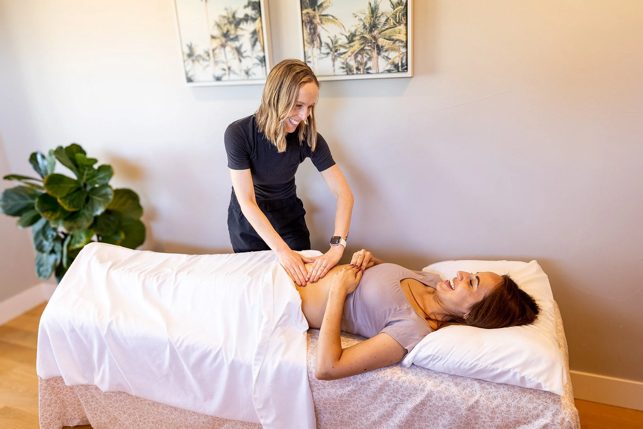 A  pelvic floor physical therapist provides holistic care to a patient laying on a treatment table while smiling and laughing