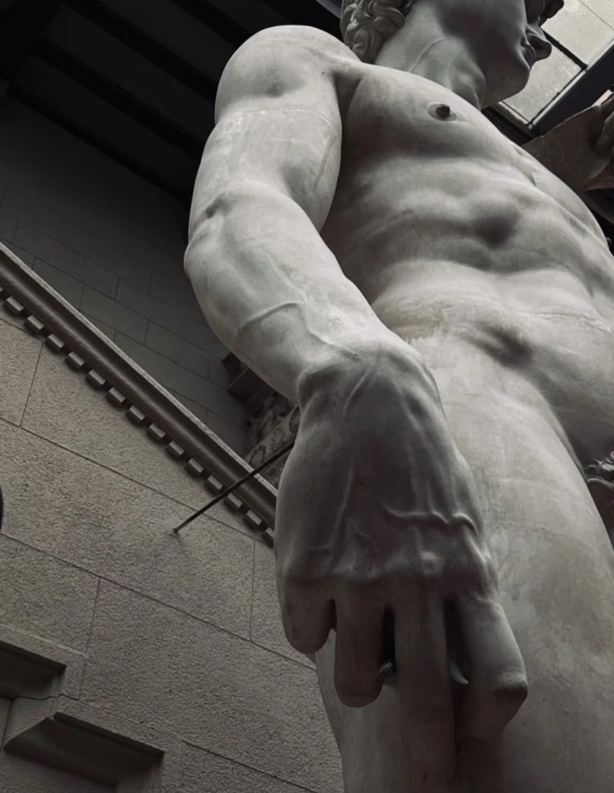 Escultura de mármol de un torso masculino sin brazos, vista desde abajo, en un edificio con ventanas y paredes de piedra.