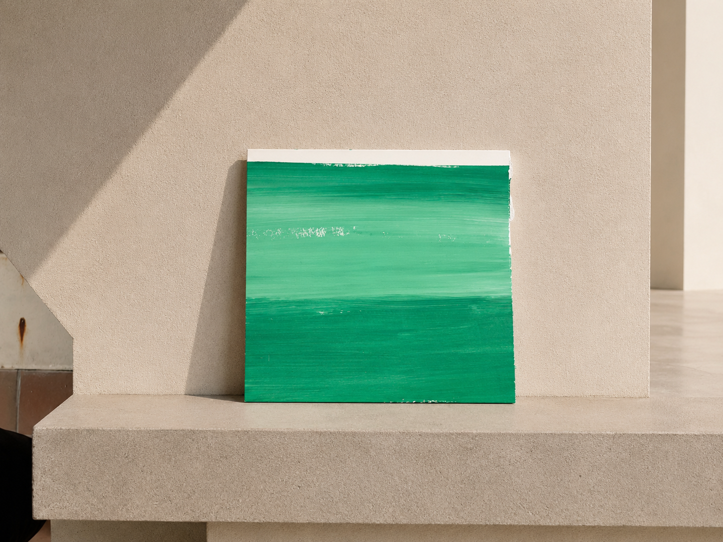 Cuadro abstracto con rayas horizontales en diferentes tonos de verde, apoyado en una repisa de color beige con sombras suaves.