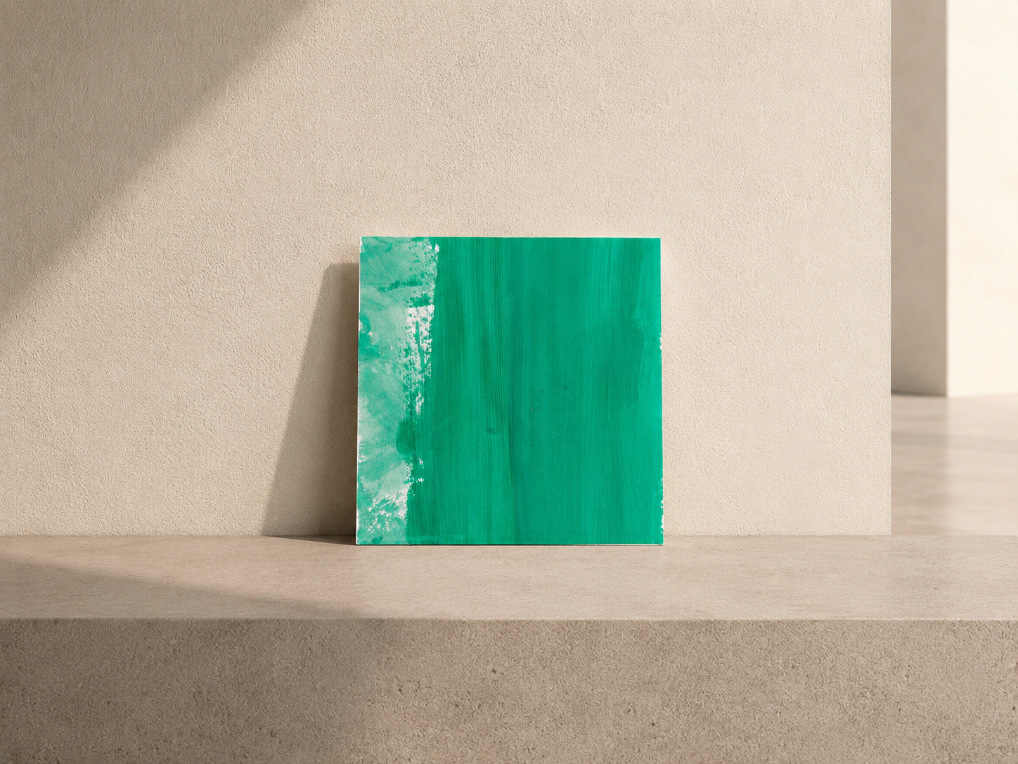 Cuadro de arte abstracto en tonos verdes apoyado en una pared beige, en un espacio con iluminación natural.