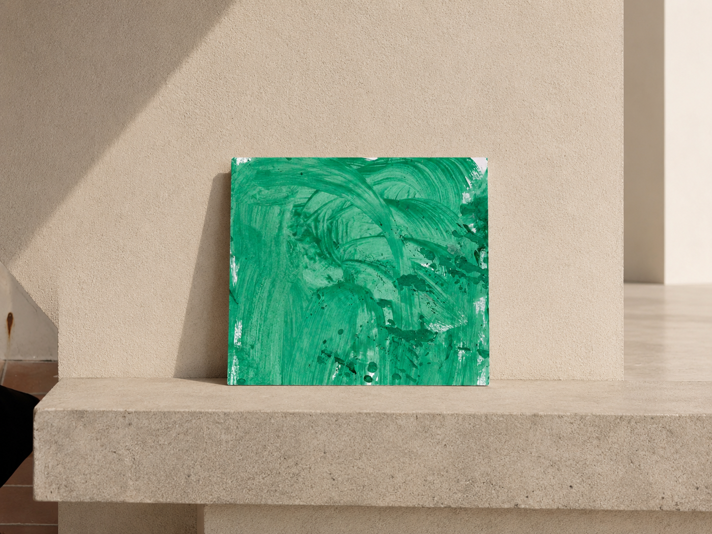 Lienzo pintado con trazos de pintura verde, colocado sobre base de piedra en un fondo beige, con sombra proyectada a la izquierda.