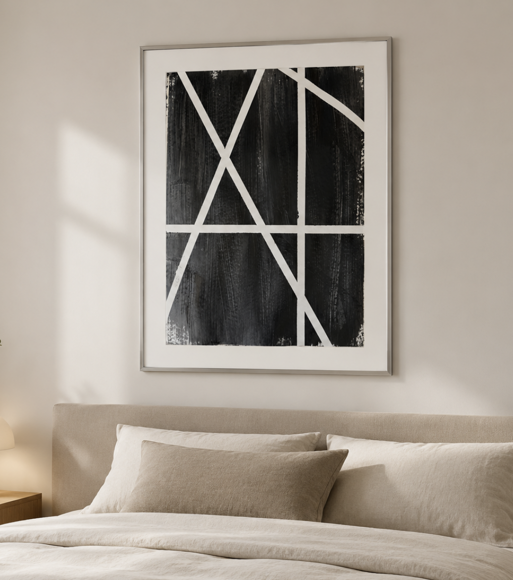 Cuadro abstracto en tonos negros y blancos colgado en pared sobre cama con cojines beige.