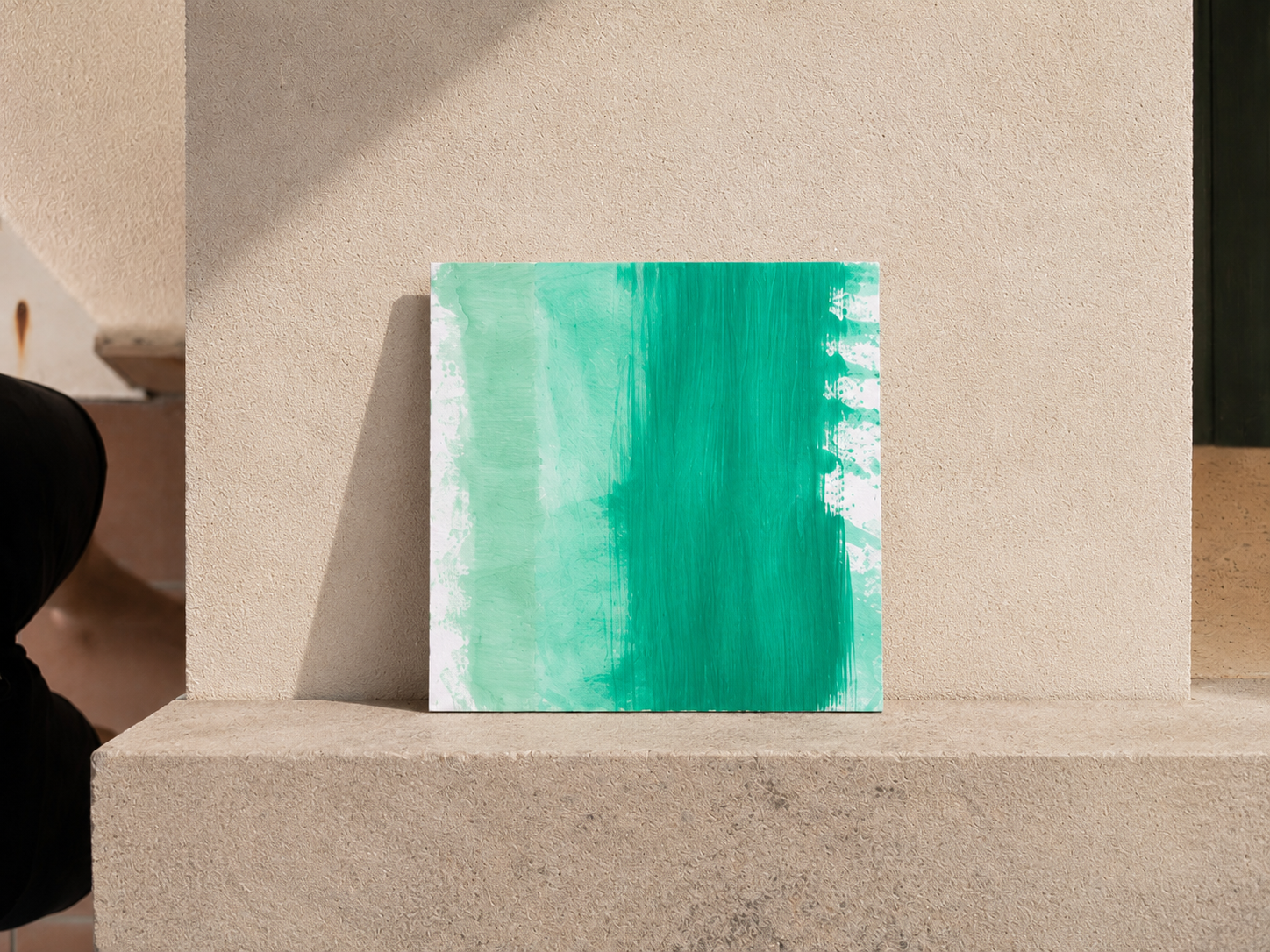 Cuadro abstracto con diferentes tonos de verde, apoyado en una estructura de concreto contra una pared beige.