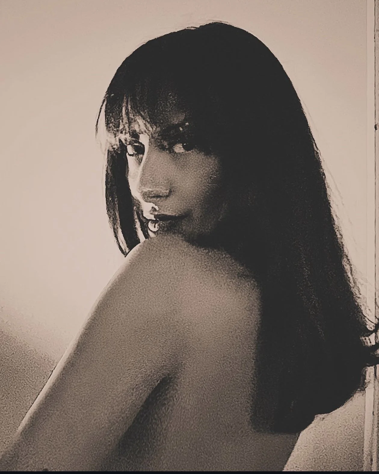 Retrato en blanco y negro de una mujer con cabello rizado y largo, mirando hacia atrás sobre su hombro, con expresión suave y seductora.