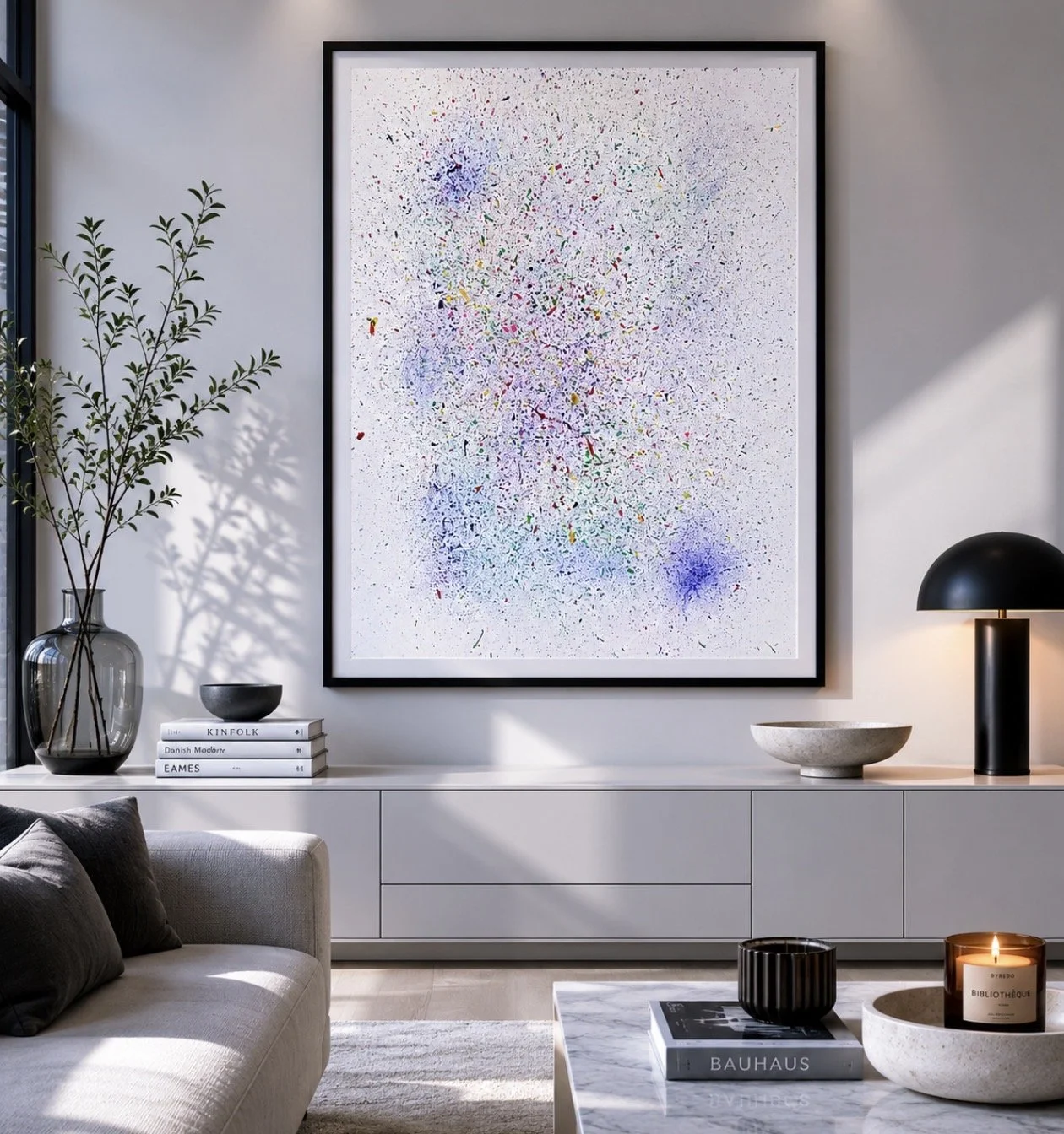 Sala moderna con cuadro abstracto en la pared, lámpara de mesa negra, jarrón grande con planta, libros, bowl y vela sobre una consola blanca.