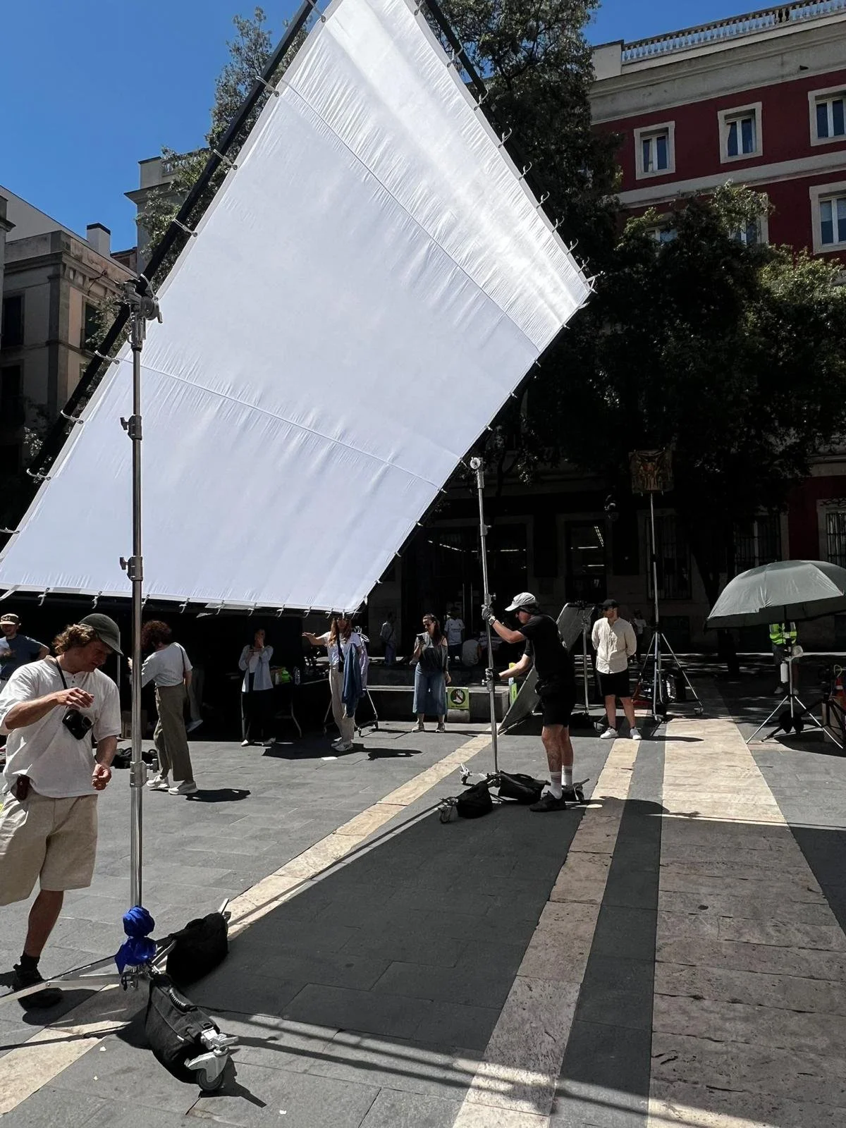 Equipo de producción colocando una pantalla grande en un evento al aire libre, con varias personas en el fondo y edificios urbanos alrededor.