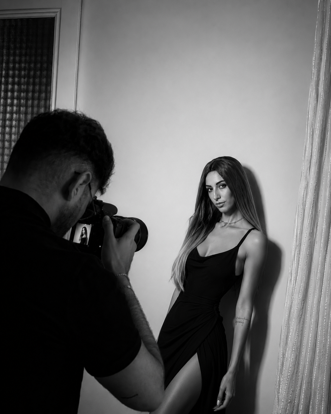 Una mujer posa para una sesión de fotos en blanco y negro mientras un fotógrafo la toma con una cámara.