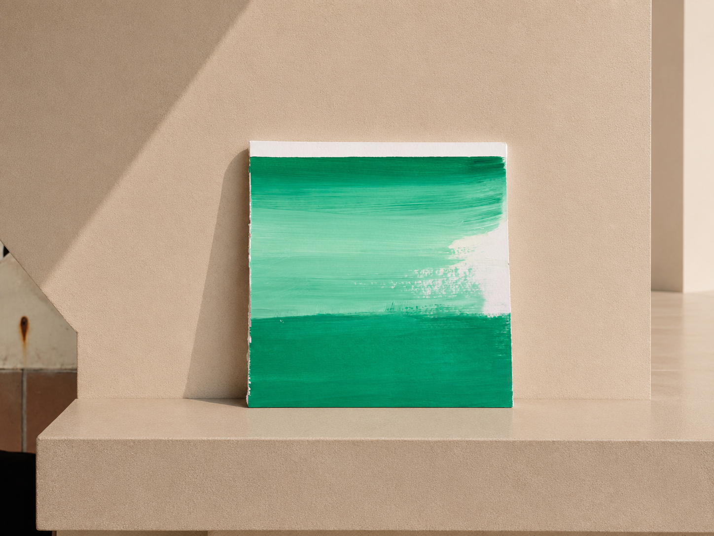 Cuadro abstracto con rayas en tonos verdes y blancos, apoyado sobre una superficie beige.