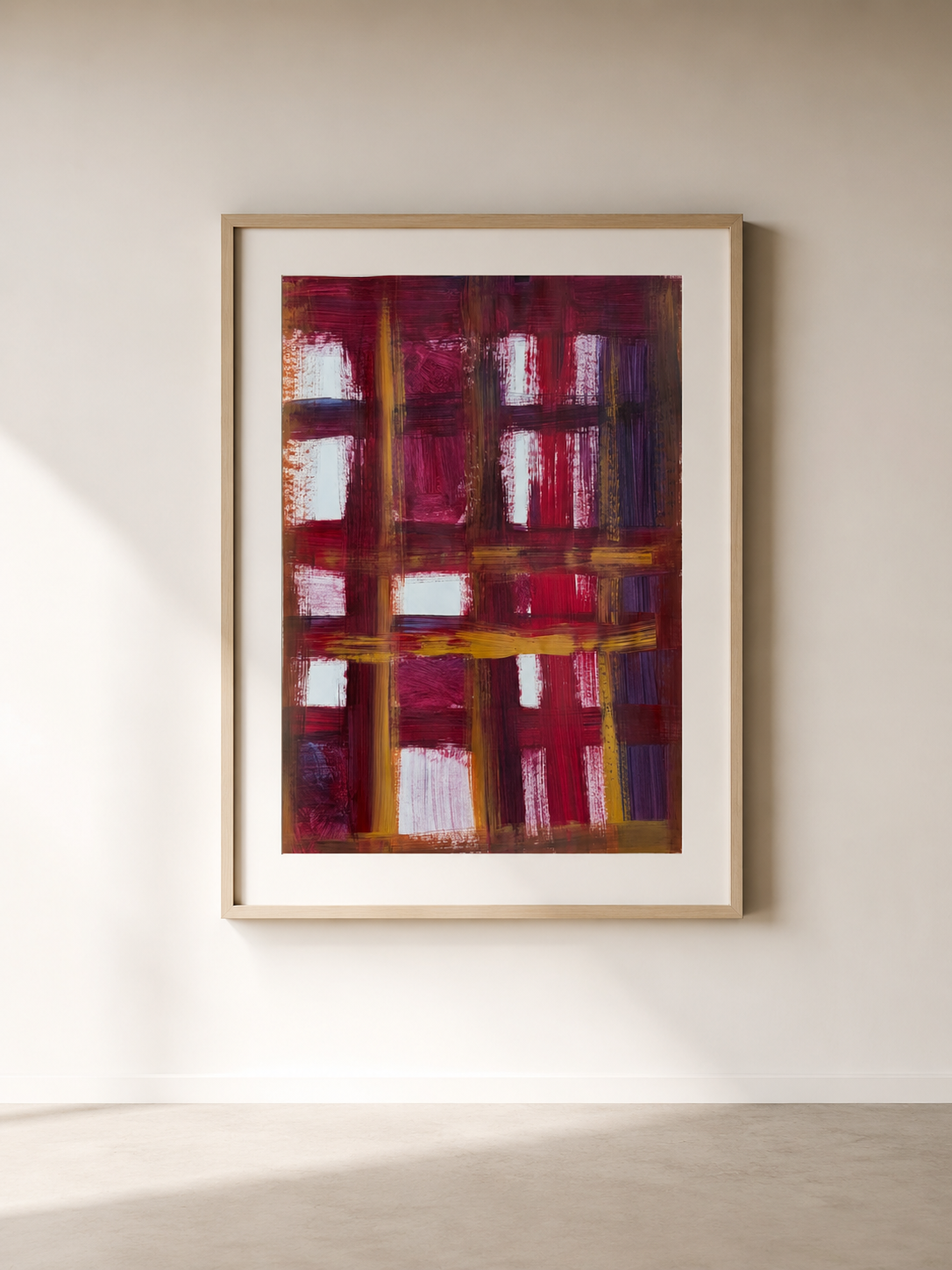 Cuadro de arte abstracto con líneas y bloques en tonos rojos, morados y dorados enmarcado en madera clara en una pared blanca en una galería.