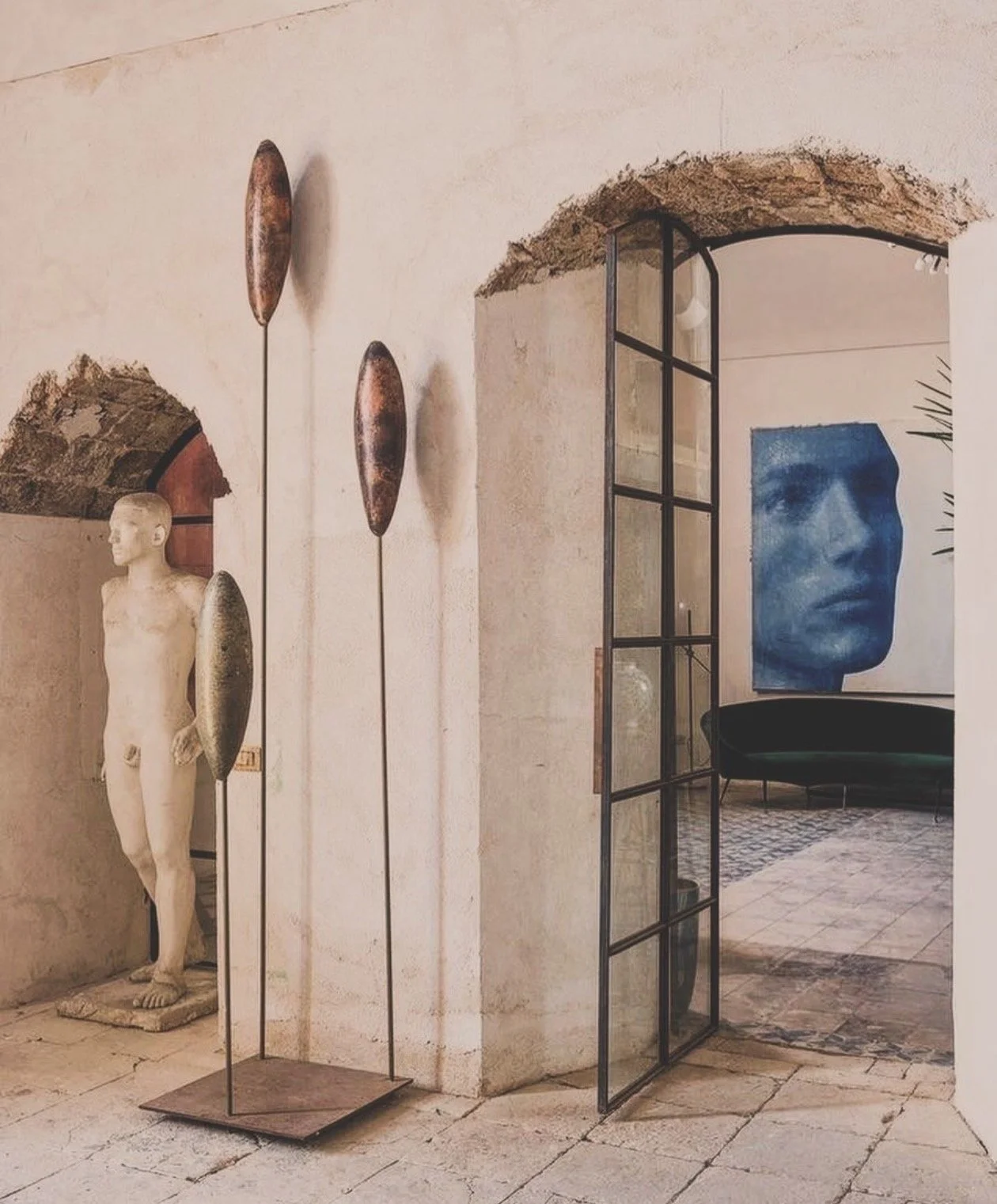Decoración interior con estatua de un niño, varias esculturas de forma alargada, un pasillo con puerta de vidrio, y arte en la pared