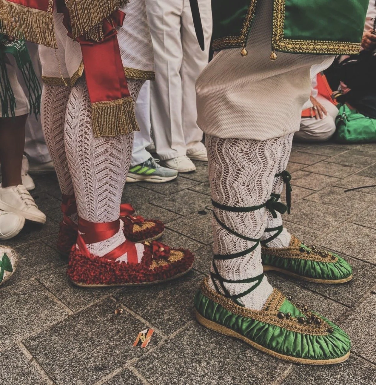 Personas con ropa tradicional y sandalias decoradas, algunas con calcetines de encaje y cintas, en una celebración o evento cultural.