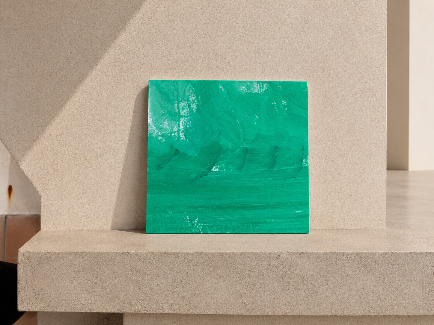 Cuadro abstracto de color verde en un soporte beige en una pared.