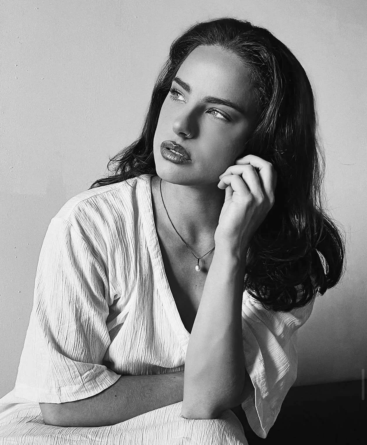 Retrato en blanco y negro de una mujer con cabello rizado suelto y con una expresión pensativa, usando una blusa clara y un collar con perla.