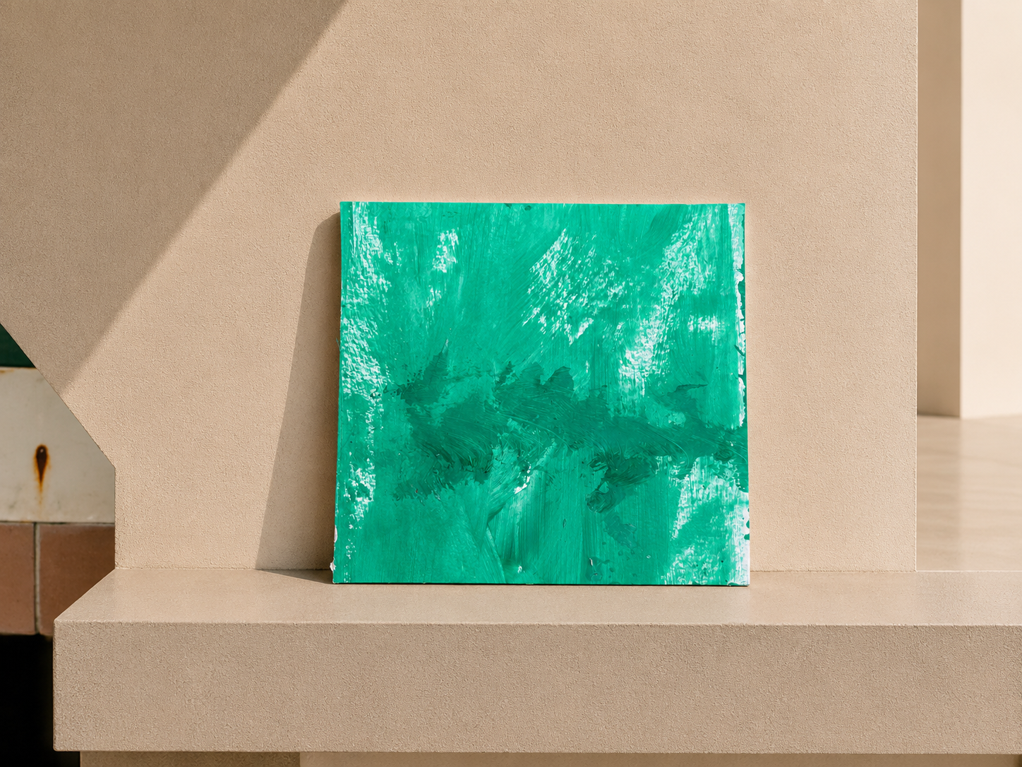 Pintura abstracta en tonos verdes colocada en una repisa de color beige con sombra proyectada a la izquierda.
