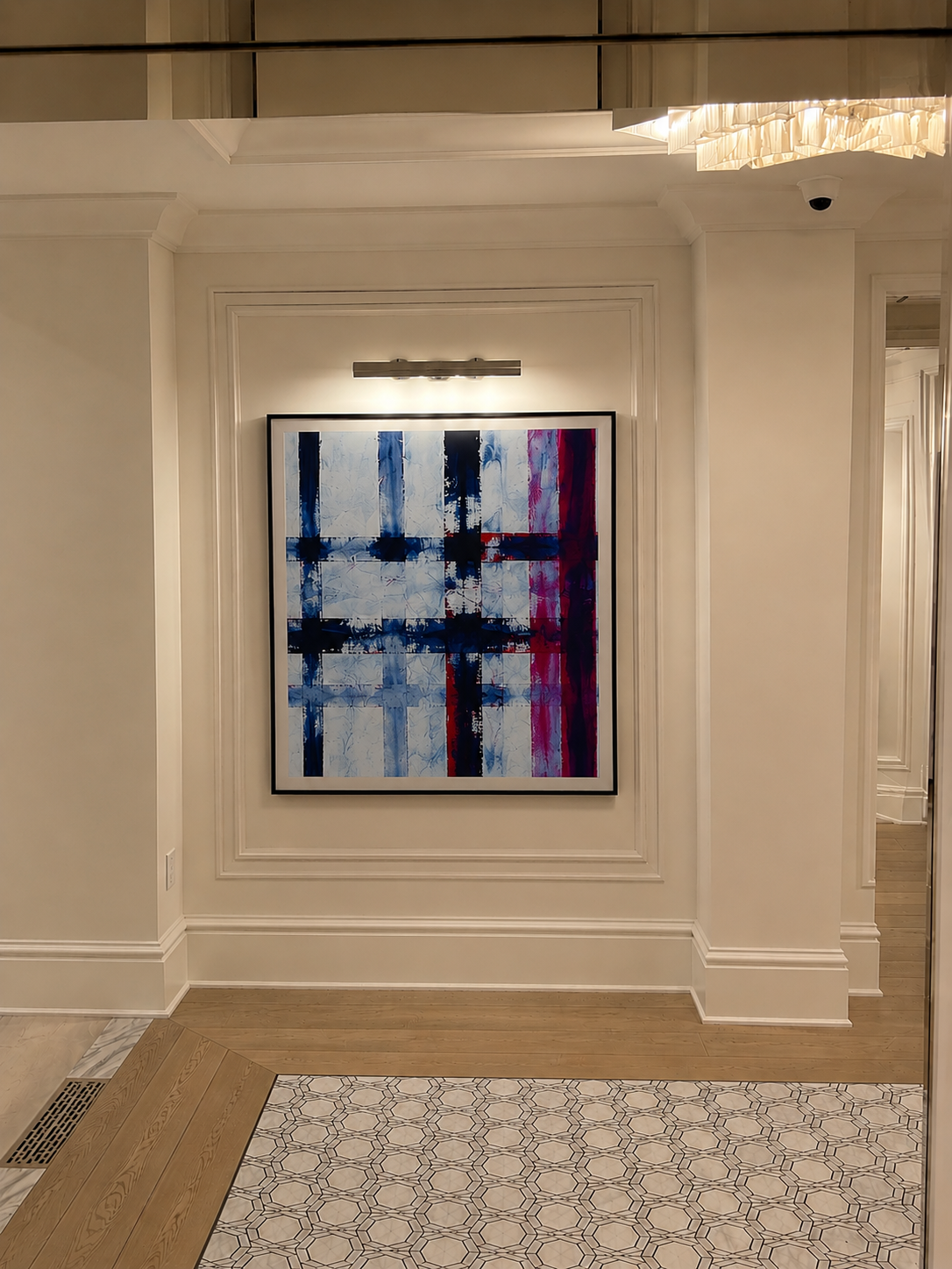 Pintura abstracta con líneas verticales en tonos azules, rojos y blancos, colgada en una pared blanca con molduras decorativas, iluminada por un foco de luz