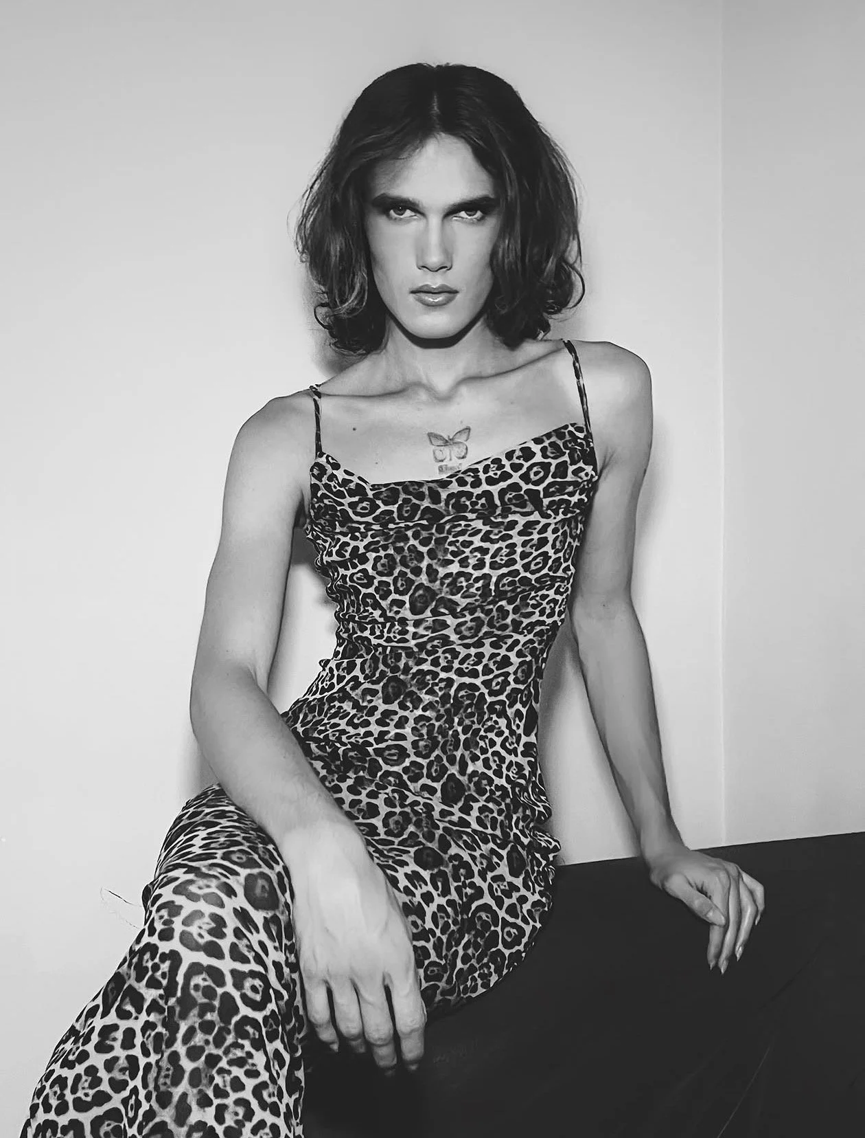 Mujer con cabello rizado y vestido ajustado con estampado de leopardo en un fondo blanco, en una pose relajada.