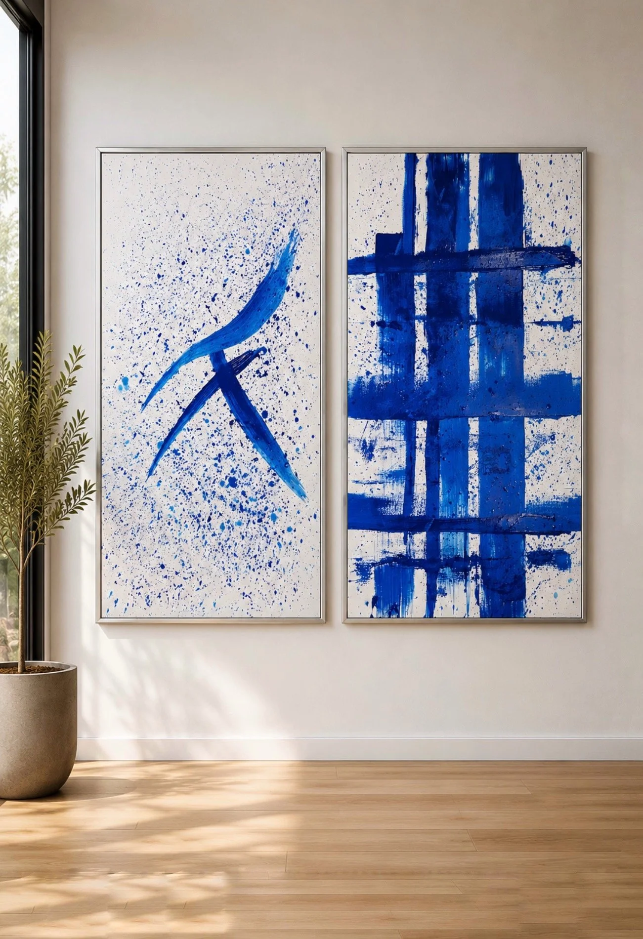 Dos cuadros abstractos en tonos azules en una pared blanca, cerca de una planta en una maceta gris, en un ambiente con suelo de madera natural.