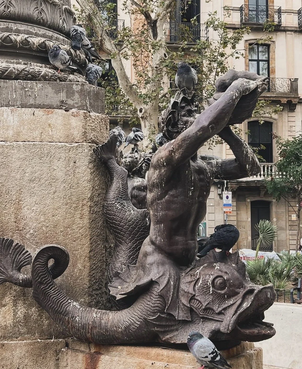 Escultura de un árbol con diferentes animales como pájaros y una serpiente en una plaza urbana.