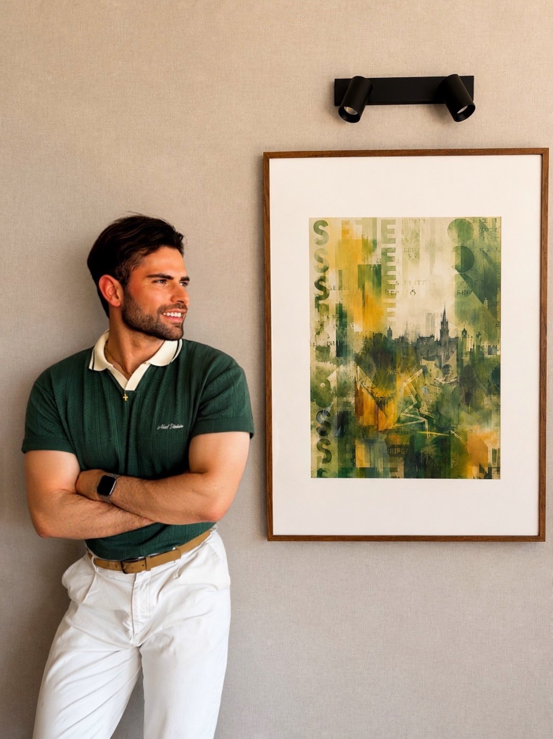 Hombre con camiseta verde y pantalones blancos, con brazos cruzados, mirando a la izquierda, junto a un cuadro abstracto en la pared.