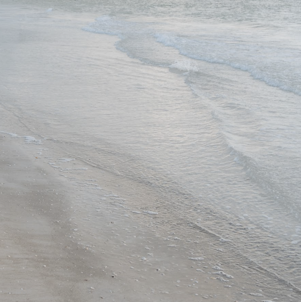 Calm ocean waves gently lapping onto a sandy beach with light-colored sand and clear water.