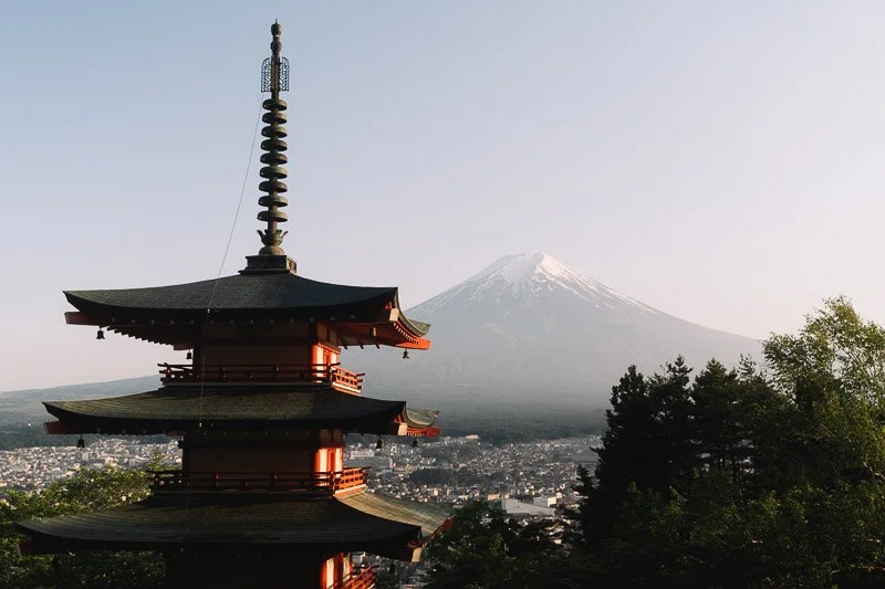 A traditional Japanese pagoda with multiple tiers, overlooking a city with Mount Fuji in the background, snow-capped and towering over the landscape.