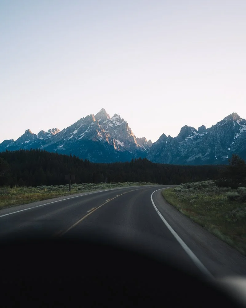 Scenic view of a winding road leading towards snow-capped mountains during dusk or dawn.
