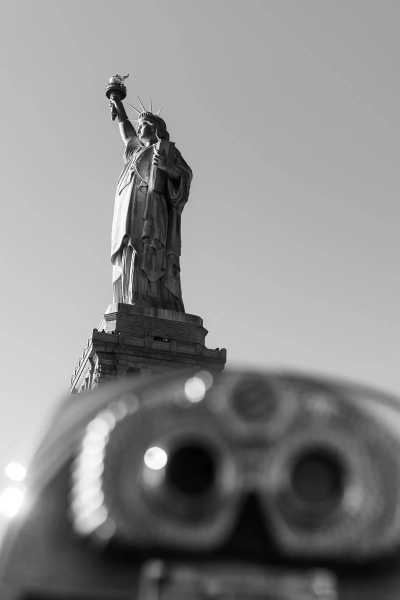 Black and white photo of the Statue of Liberty taken from below, with a blurred top of a skull-shaped object in the foreground.