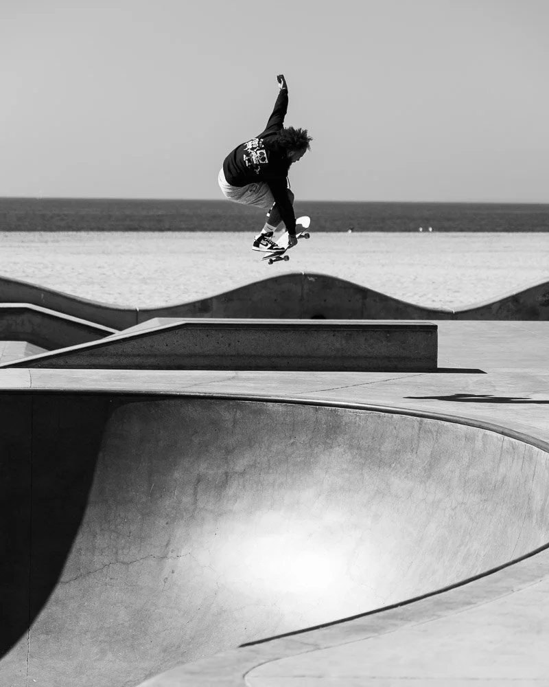 A person skateboarding in a skate park near the beach, performing a trick in mid-air.