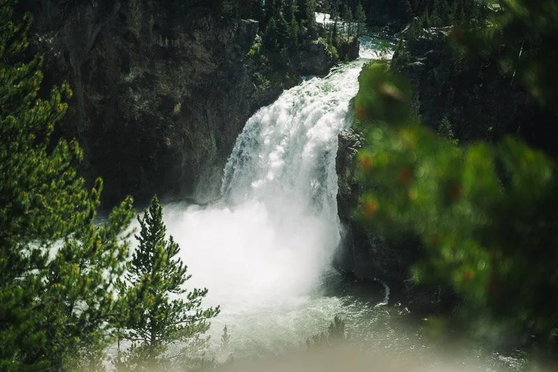 Waterfall cascading down rocky cliffs surrounded by green trees.