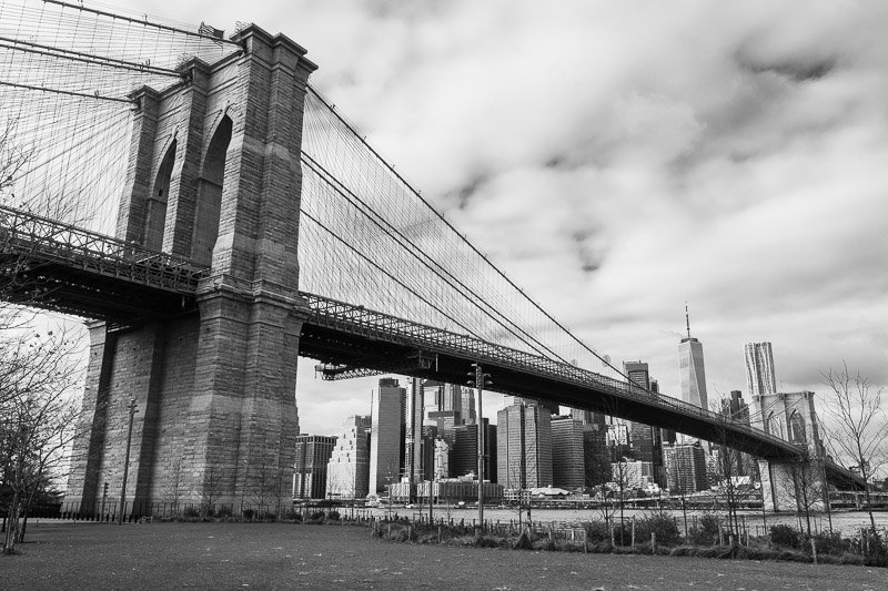 Black and white photo of the Brooklyn Bridge with Manhattan skyline in the background.